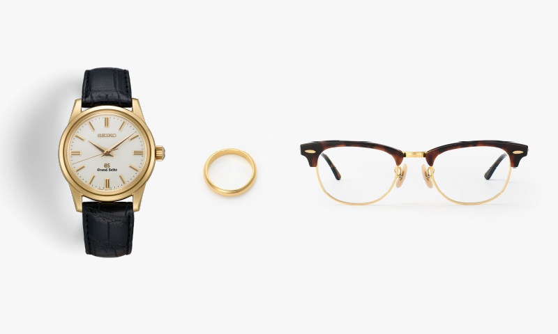 Photo of a gold Grand Seiko, gold ring, tortoiseshell and gold-rimmed glasses