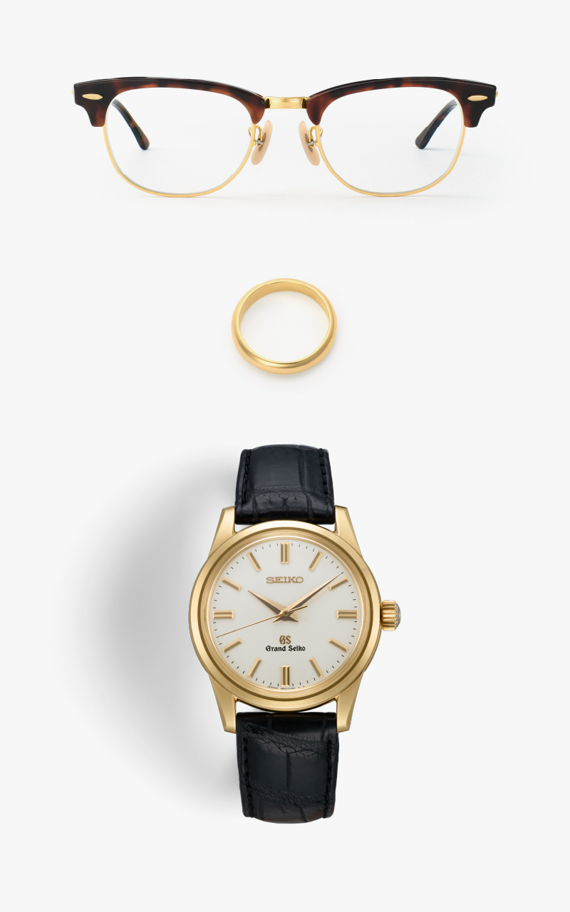 Photo of a gold Grand Seiko, gold ring, tortoiseshell and gold-rimmed glasses