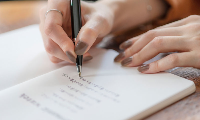 Photo of a hand writing a poem in a notebook