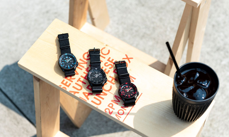 Photo of three Seiko 5 Sports watches with black dials. Indexes in blue, black, and red.