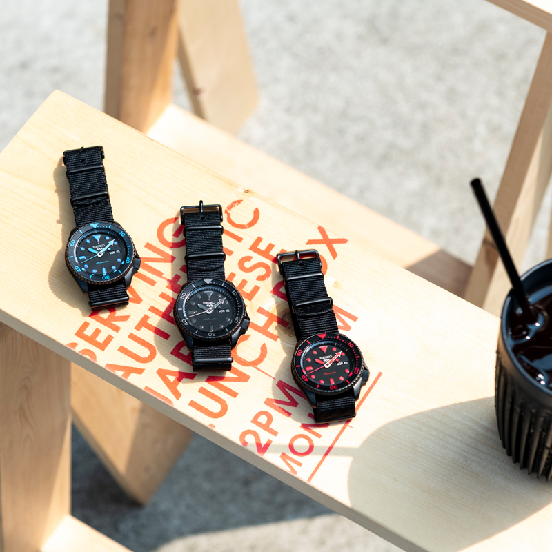 Photo of three Seiko 5 Sports watches with black dials. Indexes in blue, black, and red.